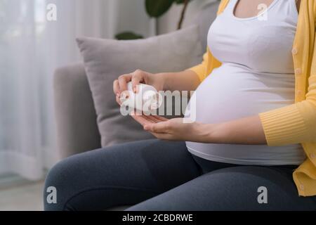 Donna incinta che tiene vaso di plastica con pillole, prendendo vitamine e minerali Foto Stock