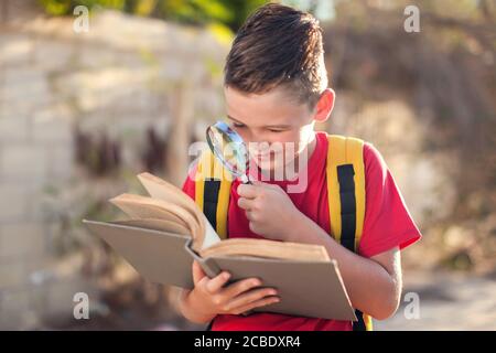 Allievo con libro e lente d'ingrandimento all'aperto. Ritorno a scuola. Bambini e concetto di istruzione Foto Stock