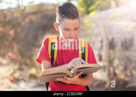 Allievo con libro e lente d'ingrandimento all'aperto. Ritorno a scuola. Bambini e concetto di istruzione Foto Stock