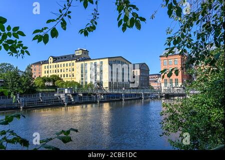 Vista verso lo storico paesaggio industriale a trascina su a. Giornata di sole nel mese di agosto 2020 dal parco cittadino Abackarna lungo Fiume Motala a Norrkoping Svezia Foto Stock