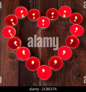 Vista dall'alto delle candele rosse che bruciano il tè che formano un cuore forma su una superficie di legno Foto Stock