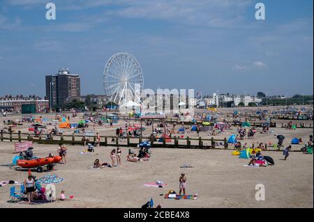 Littlehampton, West Sussex, Regno Unito, 12 agosto 2020. Turistico sulla spiaggia sul lungomare di Littlehampton con la ruota panoramica sul verde. Foto Stock