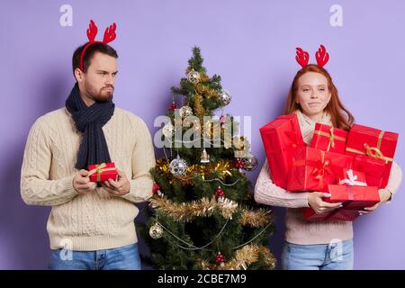 Uomo alto e sconvolto che indossa un maglione caldo casual, sciarpa a maglia a banda sul collo, con corna rosse divertenti che guardano via con espressione insoddisfatta, ottenendo s Foto Stock