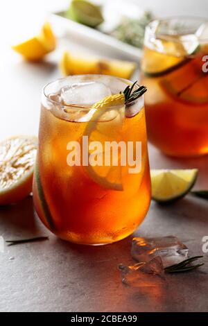 Tè freddo con limone, lime e ghiaccio guarnito con rametti di rosmarino. Bicchieri inumiditi con fette di agrumi. Foto Stock