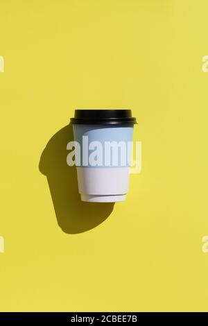 tazza monouso in carta bianca e blu per caffè o tè con ombre profonde su sfondo giallo. posa piatta. Concetto di caffè minimo. Foto Stock
