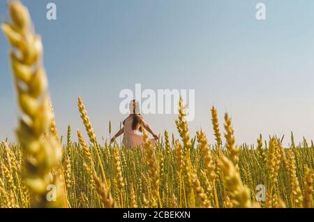 Una donna bianca in una semina rosa è nel mezzo di un campo con orecchie di grano. Foto Stock