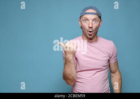 Divertente, sorpreso uomo caucasico punta il pollice al lato, aprendo la bocca con stupore e guardando con gli occhi grandi. Spazio di copia. Foto Stock