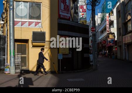 Un salarista giapponese che cammina di fronte ad un edificio giallo in una strada in Ogikubo, Tokyo, Giappone. Foto Stock