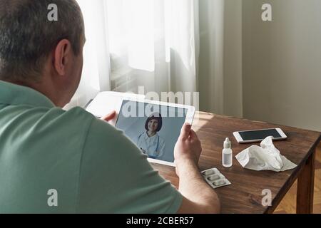 L'uomo guarda il tablet, videochiama il medico, comunica con il medico online. Telemedicina Foto Stock