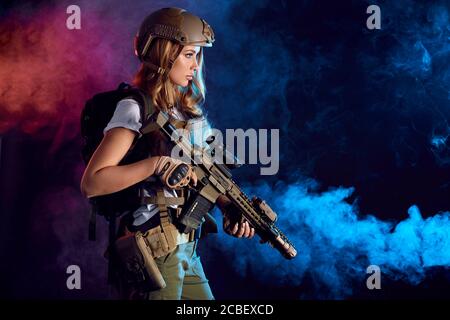 Truppa di tempesta femminile in uniforme militare camouflage protetto con casco, armatura corpo con mitragliatrice in cerca di obiettivi nelle tenebre fumose Foto Stock