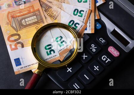 denaro con lente d'ingrandimento e calcolatrice - concetto di dichiarazione dei redditi, pianificazione del bilancio, contabilità e analisi di mercato Foto Stock