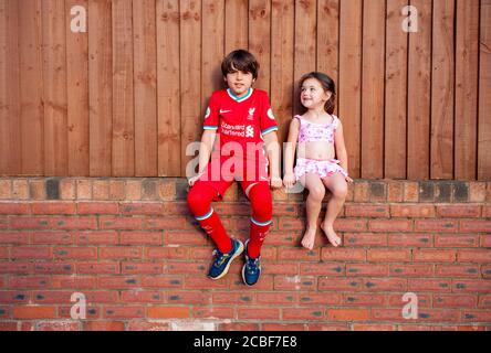 Il ragazzo caucasico di 9 anni e la sorella minore si siedono su un muro di mattoni durante l'estate del 2020. Lancashire, Regno Unito Foto Stock