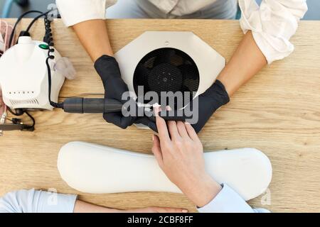 visualizza sulle mani del cliente e del master. Manicurista attento che fa le unghie belle al cliente. Tavolo in legno, attrezzatura speciale Foto Stock