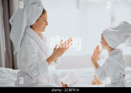 bella donna e sua figlia si siedono aggrappando le mani l'una con l'altra, indossando accappatoio e asciugamano dopo la doccia Foto Stock