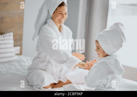 attraente femmina e bambino piccolo che va giocare le mani aggrappanti del gioco con l'altro, la madre cute guarda il bambino in accappatoio e asciugamano Foto Stock