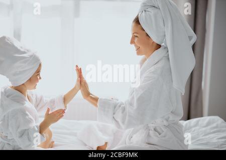 gioco di famiglia a casa. bella madre amichevole e sua figlia sedersi aggrappando le mani, giocare con l'altro, indossando accappatoio bianco e asciugamano Foto Stock