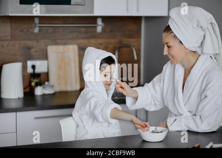 concetto di bellezza. la madre attenta usa le macchie per gli occhi e la figlia in maschera anche. genitori e bambini interessati alle procedure di bellezza Foto Stock