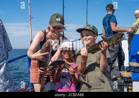 Malmo, Svezia - 6 agosto 2020: Una famiglia in un viaggio di pesca mostra il loro pescato fresco di merluzzo. Oceano blu e cielo sullo sfondo Foto Stock