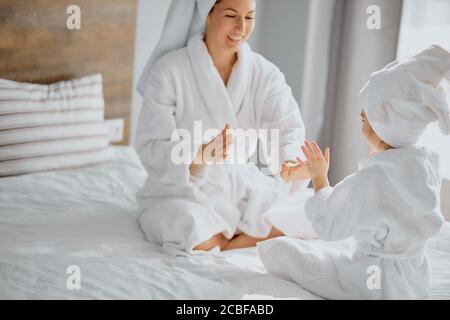 donna positiva e sua figlia si siedono aggrappando le mani l'una con l'altra, indossando accappatoio e asciugamano dopo la doccia Foto Stock