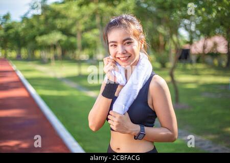 Bella giovane donna asiatica si ferma a spazzare via il sudore dopo la sua mattina corri su una pista da corsa all'aperto una mattina luminosa e soleggiata Foto Stock