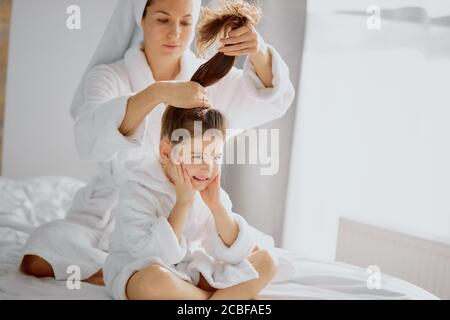 bella femmina e figlia si siedono dopo la doccia insieme, madre in ordine i capelli della figlia Foto Stock