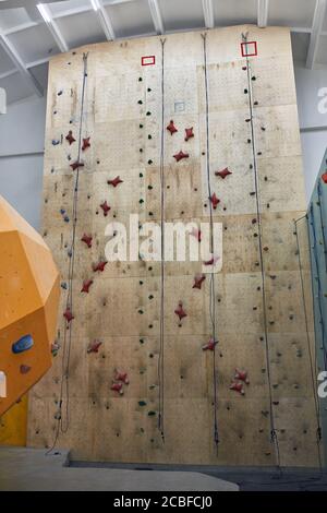 Foto verticale di parete artificiale alta arrampicata, pannello di legno con coloratissime stive e corde, palestra coperta di bouldering. Concetto di sport e stile di vita attivo Foto Stock
