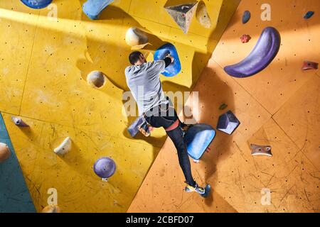 Vista ad angolo basso di alpinista atletico irriconoscibile senza allenamento all'interno dell'avambraccio, arrampicata grande parete di roccia gialla, si sente piena di motivazione e Foto Stock