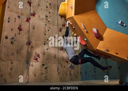 Vista laterale del boulderer professionista fisicamente disabili allenarsi duro dopo il riscaldamento di esercizi, arrampicarsi su parete di roccia artificiale, gode il suo ex Foto Stock