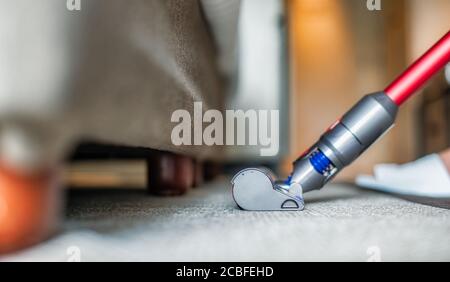 Aspirapolvere moderno durante l'aspirazione. Donna che usa un aspirapolvere mentre pulisce la moquette in casa. Concetto di pulizia della casa. Foto Stock