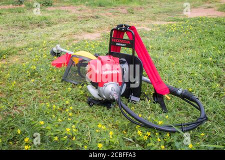 Un rasaerba Honda rosso modello UMR 435t e uno schermo facciale di sicurezza giallo sono sul terreno pieno di erbacce dopo il lavoro. Hua Hin, Thail Foto Stock