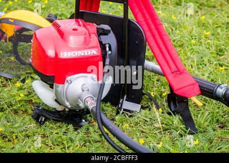 Un rasaerba Honda rosso modello UMR 435t e uno schermo facciale di sicurezza giallo sono sul terreno pieno di erbacce dopo il lavoro. Hua Hin, Thail Foto Stock