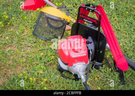 Un rasaerba Honda rosso modello UMR 435t e uno schermo facciale di sicurezza giallo sono sul terreno pieno di erbacce dopo il lavoro. Hua Hin, Thail Foto Stock