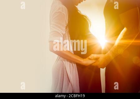 Praenant moglie coppia amante in piedi tenendo cura della mano insieme wtih sole per sempre stare da me e essere un buon amore per sempre concetto. Foto Stock