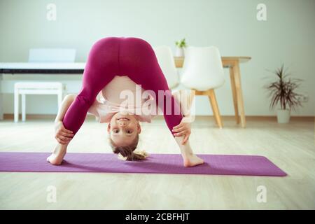 Ragazza del bambino felice graziosa che ha divertimento che fa le esercitazioni di yoga a. casa Foto Stock