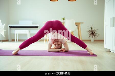 Ragazza del bambino felice graziosa che ha divertimento che fa le esercitazioni di yoga a. casa Foto Stock