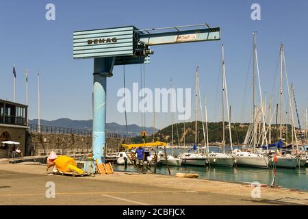 Una gru Demag per il carico e lo scarico di merci nel porto di Lerici con barche a vela ormeggiate in estate, la Spezia, Liguria, Italia Foto Stock