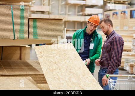 esperto nel suo campo, lavoratore di magazzino consultare il cliente, mostrare tavola di legno e parlare di tutti i vantaggi di esso Foto Stock