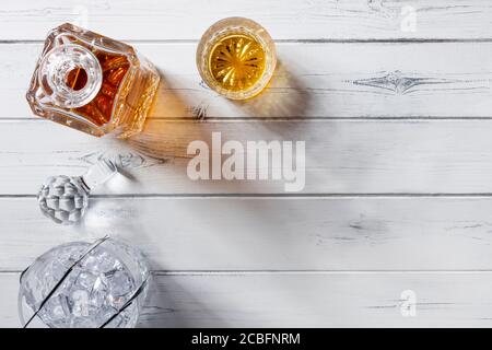 Vista di un vetro di cristallo e di un decanter pieno di whisky dorato, e secchio di ghiaccio di cristallo, sparato dall'alto su uno sfondo di legno bianco afflitto con spazio Foto Stock