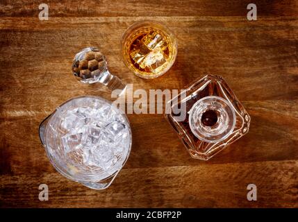 Vista di un vetro di cristallo e di un decanter pieno di whisky dorato, e secchio di ghiaccio, sparato dall'alto su uno sfondo di legno scuro Foto Stock