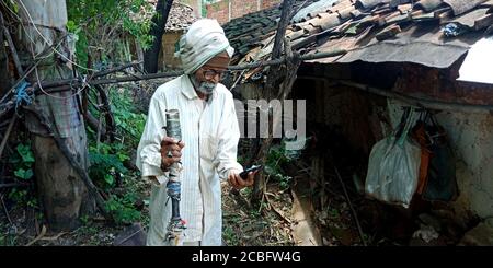 DISTRETTO KATNI, INDIA - 20 AGOSTO 2019: Un vecchio uomo di villaggio indiano che guarda lo smartphone, tenendo il concetto di bastone sulla mano per l'educazione digitale della gente asiatica Foto Stock