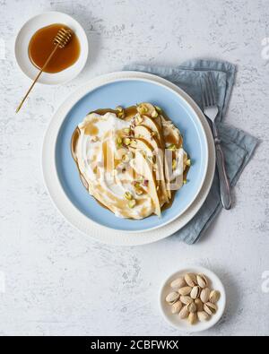 Ricotta con pere, pistacchi e sciroppo di miele o acero su piatto blu su tavola bianca. Foto Stock