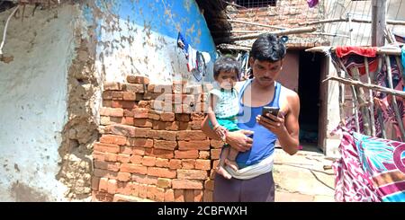 DISTRETTO KATNI, INDIA - 20 AGOSTO 2019: Un uomo indiano di villaggio che opera il telefono intelligente tenendo il bambino a portata di mano, concetto per l'apprendimento digitale della gente asiatica. Foto Stock