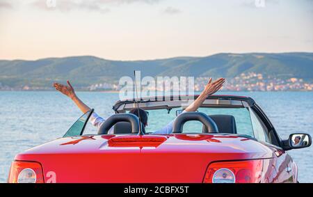 Donna in una macchina rossa alzò le mani sul mare. Foto Stock