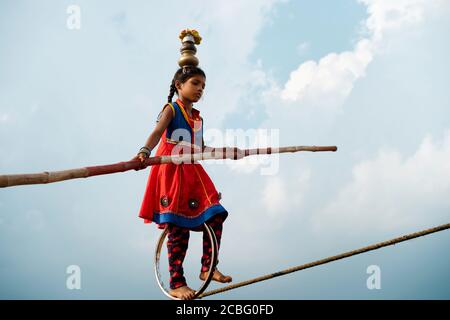 Giovane ragazza usiing poke di bambù e cerchio di ruota per negoziare abilmente tightrope il 07 novembre 2019 a Pushkar, Rajasthan, India. Foto Stock