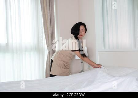 Giovane bella cameriera asiatica che sistemava la coperta sul letto camera d'albergo Foto Stock