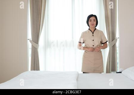 La giovane cameriera asiatica nella camera d'albergo che guarda fotocamera Foto Stock