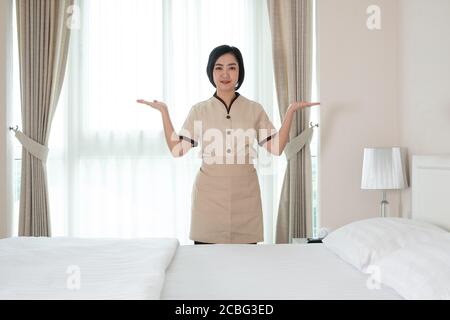La giovane cameriera asiatica nella camera d'albergo che guarda fotocamera Foto Stock