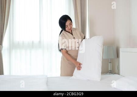 Giovane bella cameriera asiatica che sistemava il cuscino sul letto camera d'albergo Foto Stock