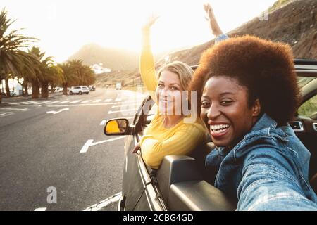 Giovani donne felici che prendono selfie facendo viaggio su strada - Viaggi ragazze che si divertono a guidare in un'auto convertibile alla moda scoprendo nuove luoghi Foto Stock