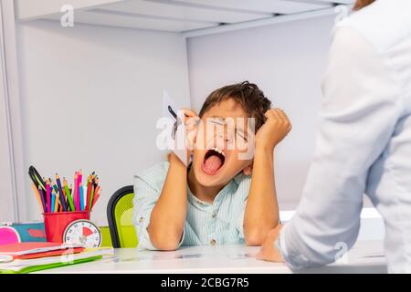 Il bambino autistico strappa i capelli e urla esprimendo emozioni negative mentre numeri di apprendimento seduti dall'insegnante Foto Stock